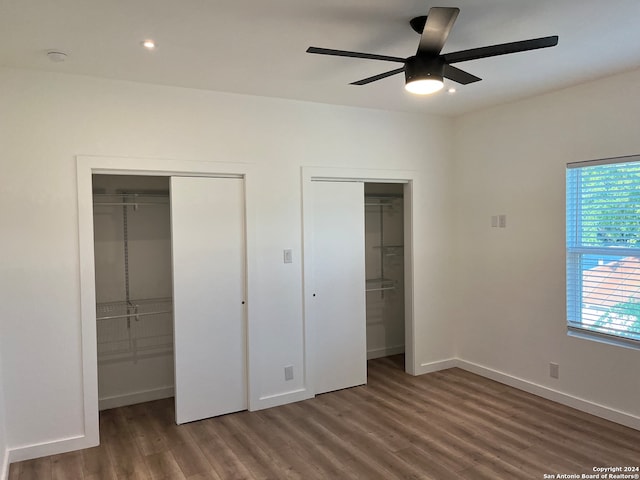 unfurnished bedroom with multiple closets, ceiling fan, and dark wood-type flooring