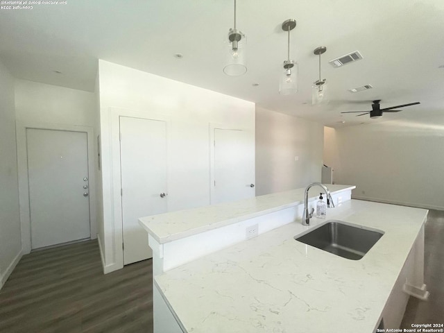 kitchen featuring ceiling fan, sink, a center island with sink, decorative light fixtures, and light stone countertops