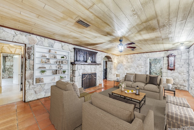 living room featuring built in shelves, ceiling fan, a stone fireplace, and wood ceiling