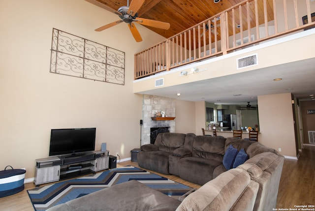 living room featuring a stone fireplace, a towering ceiling, ceiling fan, and hardwood / wood-style flooring