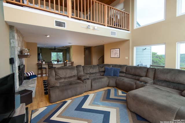 living room featuring hardwood / wood-style floors, a high ceiling, a large fireplace, and ceiling fan