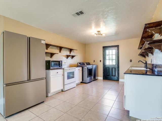 kitchen featuring white cabinets, light tile patterned floors, sink, washing machine and clothes dryer, and appliances with stainless steel finishes