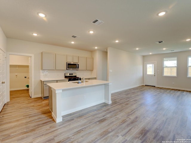 9918 Forestier Grn, San Antonio, TX 78221 - kitchen with stainless steel appliances, light countertops, light wood-style floors, baseboards, and an island with sink