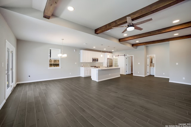 unfurnished living room featuring beam ceiling, a barn door, ceiling fan with notable chandelier, and dark hardwood / wood-style floors