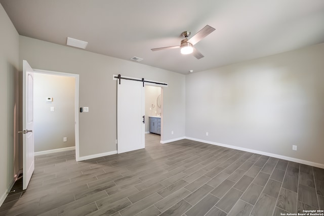 unfurnished bedroom with a barn door, ensuite bath, ceiling fan, and dark wood-type flooring