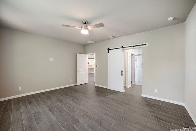 unfurnished bedroom featuring a barn door, ceiling fan, and dark hardwood / wood-style floors