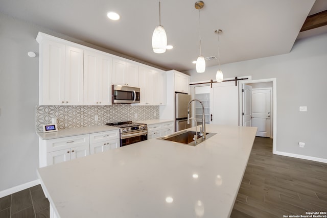 kitchen with a barn door, dark hardwood / wood-style floors, pendant lighting, a center island with sink, and appliances with stainless steel finishes