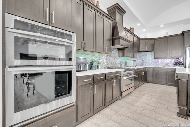 kitchen with premium range hood, lofted ceiling, dark brown cabinets, appliances with stainless steel finishes, and decorative backsplash