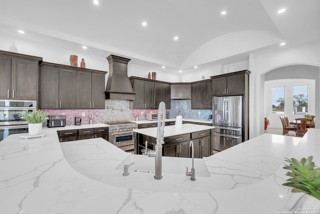 kitchen with stainless steel appliances, light stone counters, vaulted ceiling, and custom range hood