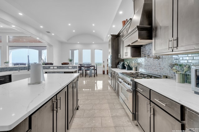 kitchen with high end range, custom exhaust hood, light stone counters, and a wealth of natural light