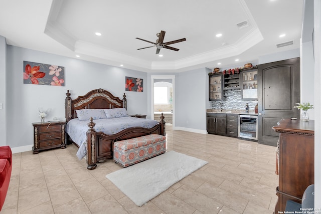 bedroom with wine cooler, bar area, connected bathroom, a raised ceiling, and ceiling fan