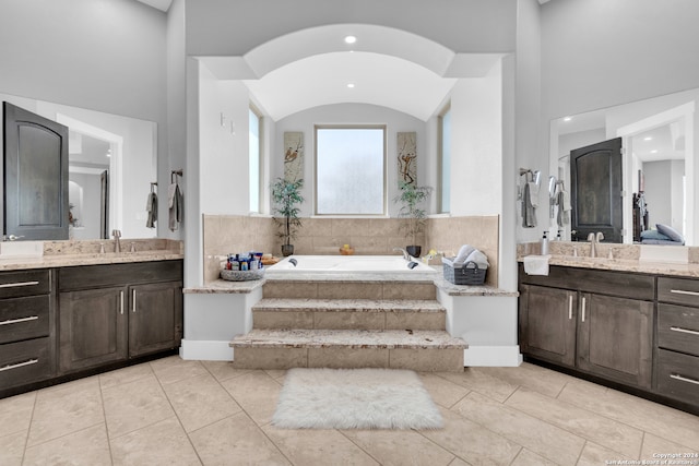 bathroom featuring tiled bath, vanity, vaulted ceiling, and tile patterned floors