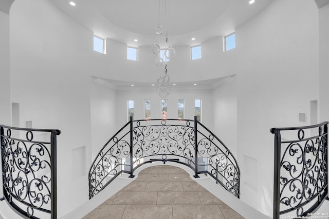 stairway featuring tile patterned flooring, a towering ceiling, a chandelier, and crown molding