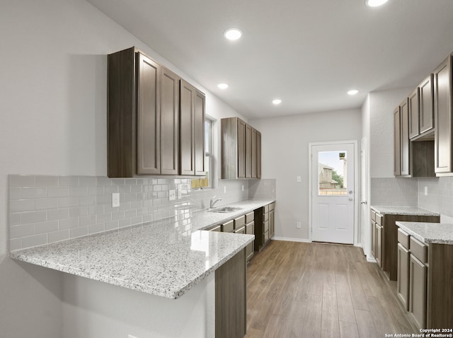 kitchen featuring kitchen peninsula, tasteful backsplash, wood-type flooring, dark brown cabinets, and light stone countertops