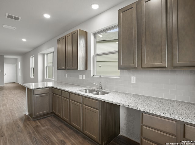 kitchen with dark hardwood / wood-style floors, sink, kitchen peninsula, backsplash, and light stone countertops