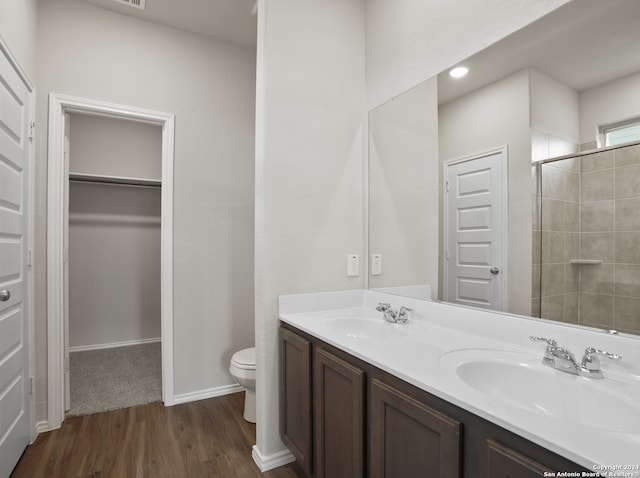 bathroom with wood-type flooring, a shower with door, vanity, and toilet