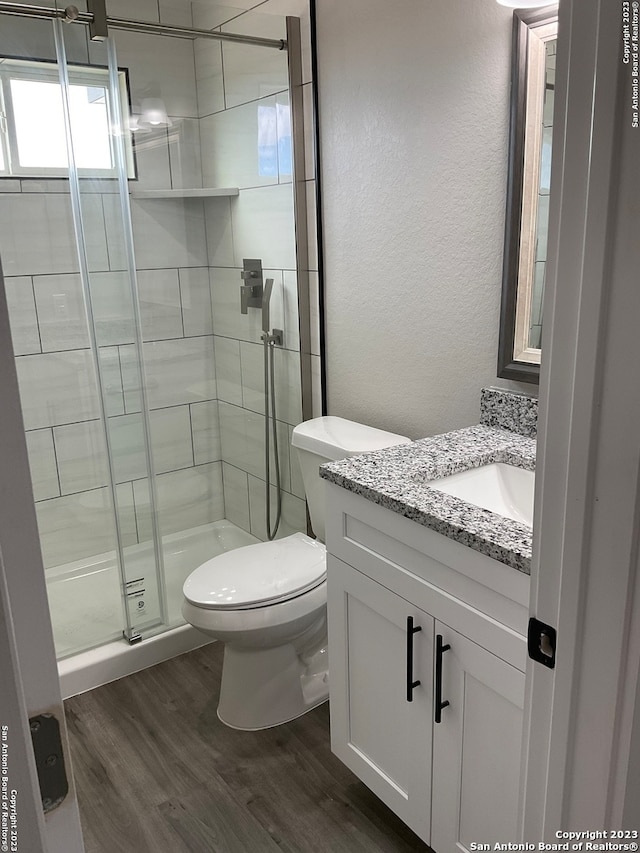 bathroom with hardwood / wood-style floors, vanity, toilet, and a shower with shower door