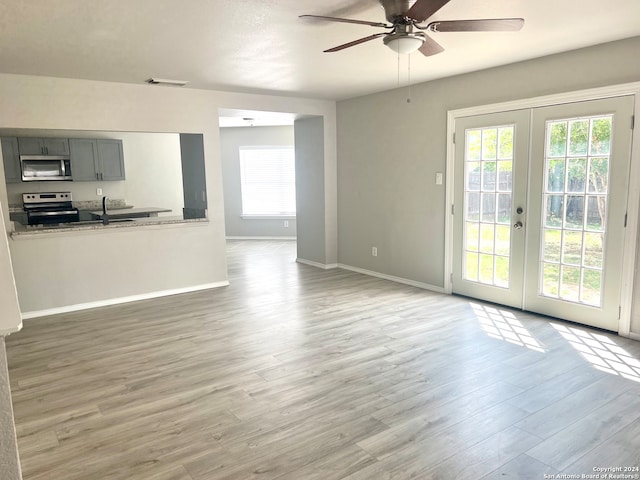 unfurnished living room featuring ceiling fan, french doors, light hardwood / wood-style floors, and a healthy amount of sunlight