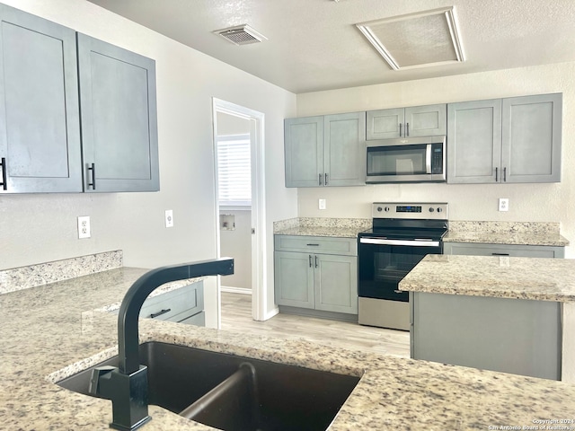 kitchen with light stone counters, appliances with stainless steel finishes, sink, and light hardwood / wood-style flooring