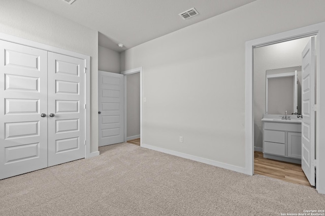 unfurnished bedroom with light colored carpet, sink, connected bathroom, and a closet