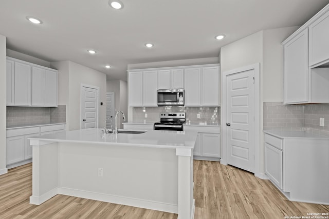 kitchen with stainless steel appliances, white cabinetry, a kitchen island with sink, and sink