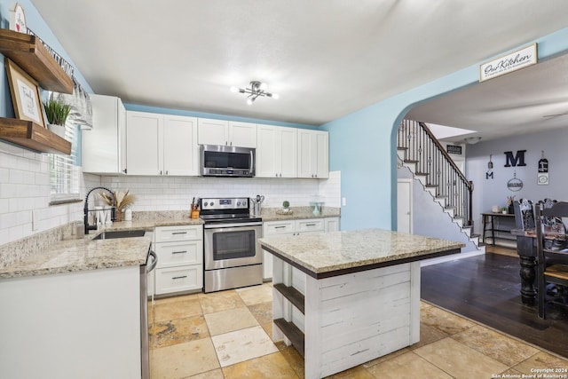 kitchen with appliances with stainless steel finishes, white cabinetry, backsplash, a kitchen island, and sink