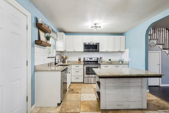 kitchen with sink, white cabinetry, appliances with stainless steel finishes, a center island, and light stone countertops