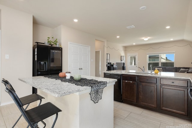 kitchen with a kitchen breakfast bar, black appliances, light stone counters, and a kitchen island with sink