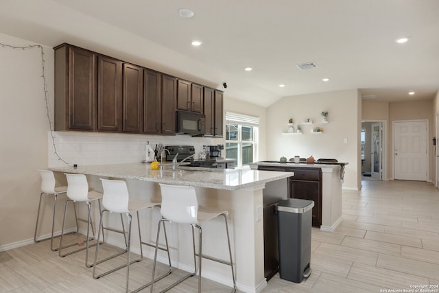 kitchen featuring light stone counters, lofted ceiling, kitchen peninsula, black appliances, and a kitchen breakfast bar