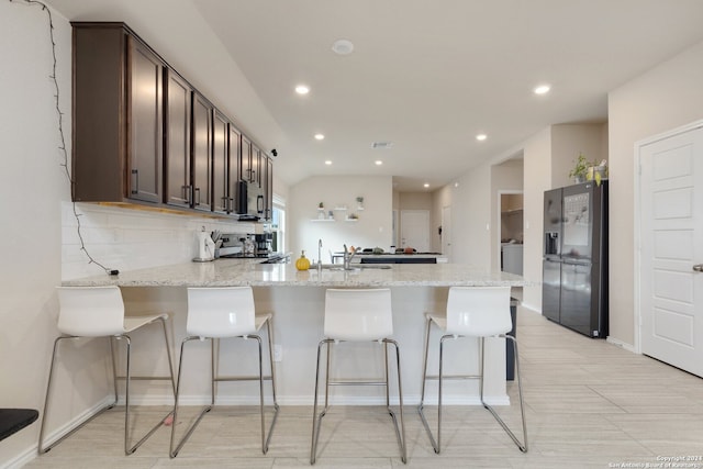 kitchen featuring light stone counters, dark brown cabinetry, black refrigerator with ice dispenser, and a breakfast bar area