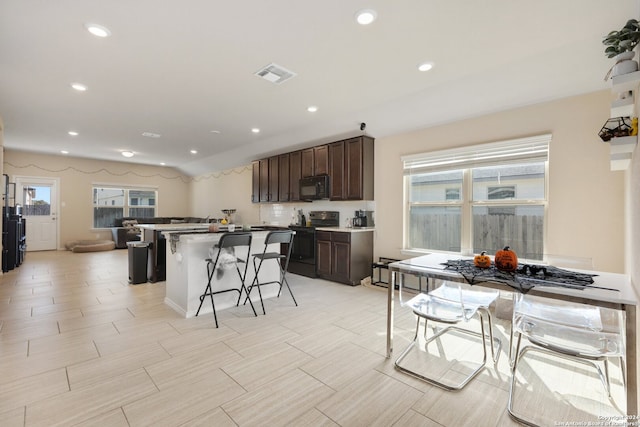 kitchen with black appliances, dark brown cabinetry, a center island, and a breakfast bar