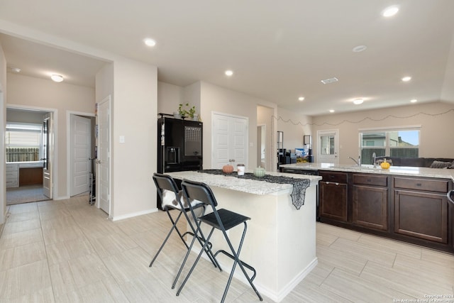 kitchen with dark brown cabinetry, light stone countertops, a breakfast bar area, and a center island with sink