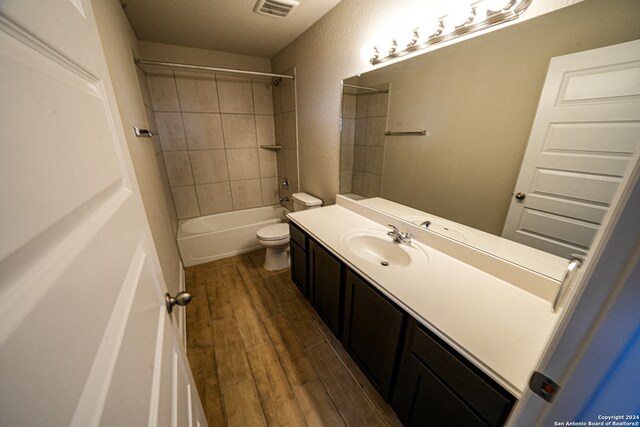 full bathroom with tiled shower / bath, vanity, hardwood / wood-style floors, and toilet