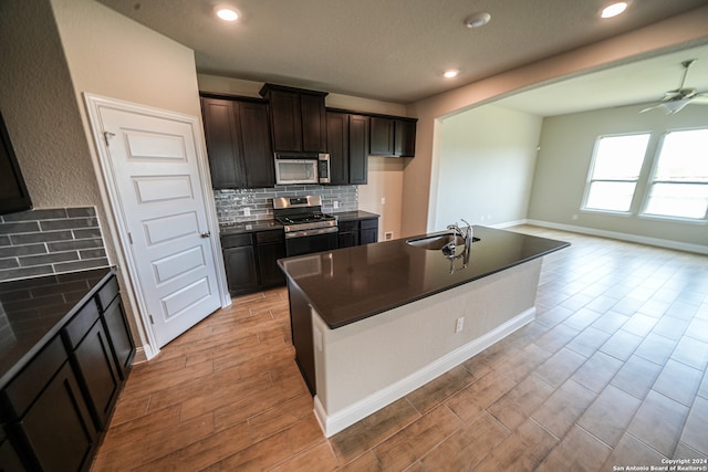 kitchen featuring ceiling fan, tasteful backsplash, a center island with sink, stainless steel appliances, and light hardwood / wood-style floors