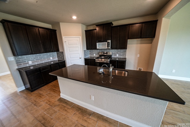 kitchen featuring appliances with stainless steel finishes, an island with sink, backsplash, dark brown cabinets, and sink