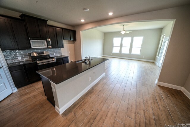 kitchen featuring ceiling fan, a center island with sink, appliances with stainless steel finishes, and light wood-type flooring