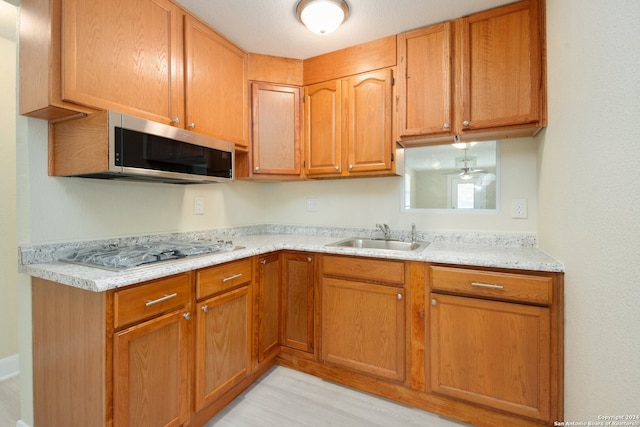 kitchen featuring appliances with stainless steel finishes, light hardwood / wood-style floors, sink, and light stone counters