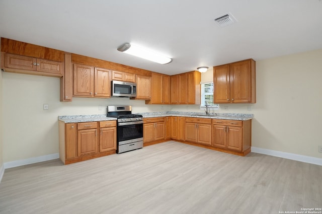 kitchen with light stone countertops, light hardwood / wood-style floors, appliances with stainless steel finishes, and sink