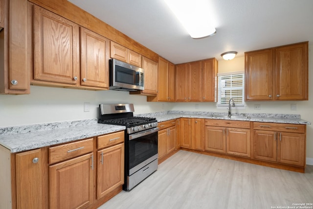 kitchen with appliances with stainless steel finishes, light stone countertops, light hardwood / wood-style floors, and sink