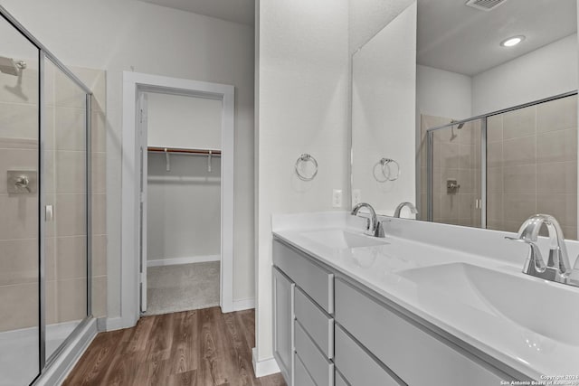 full bath with a walk in closet, a shower stall, wood finished floors, and a sink