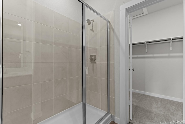 full bathroom with a spacious closet, a stall shower, and baseboards