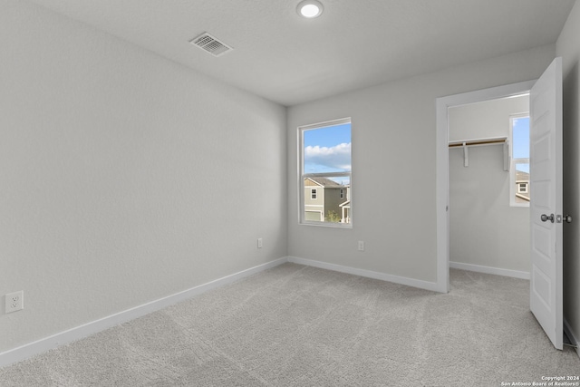 unfurnished bedroom featuring visible vents, a walk in closet, baseboards, light carpet, and a closet