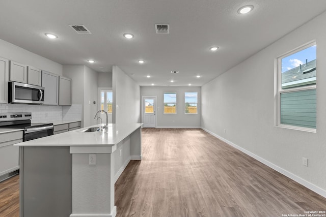 kitchen featuring gray cabinetry, a sink, tasteful backsplash, wood finished floors, and stainless steel appliances