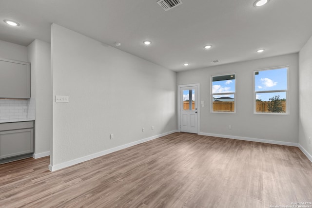 unfurnished living room with light wood-type flooring, visible vents, and baseboards