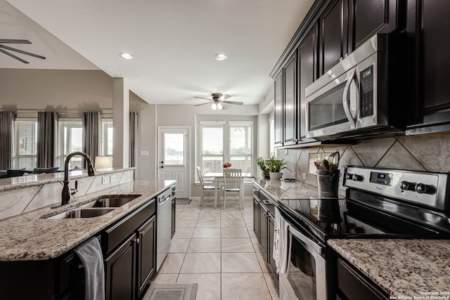 kitchen featuring backsplash, light stone countertops, stainless steel appliances, ceiling fan, and sink