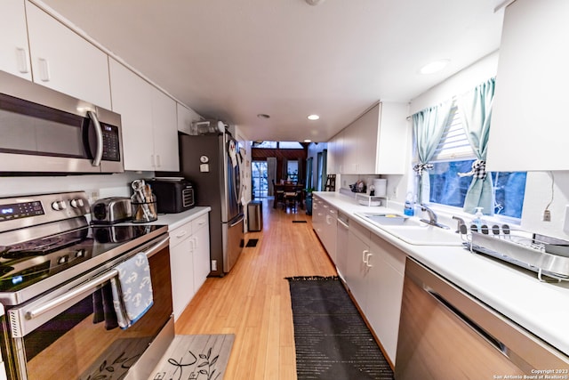 kitchen with stainless steel appliances, light wood-type flooring, sink, and white cabinetry