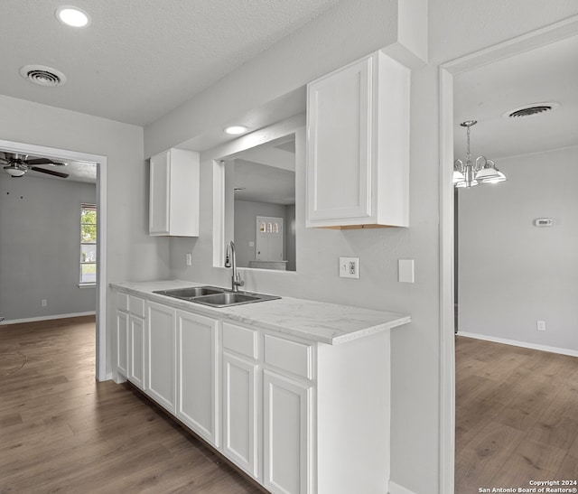 kitchen with ceiling fan with notable chandelier, white cabinets, hardwood / wood-style flooring, and sink