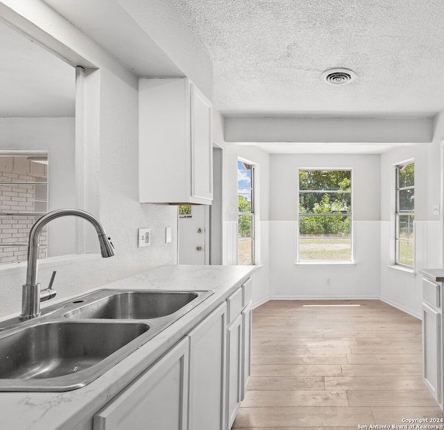 kitchen with light stone counters, sink, a textured ceiling, white cabinetry, and light hardwood / wood-style floors