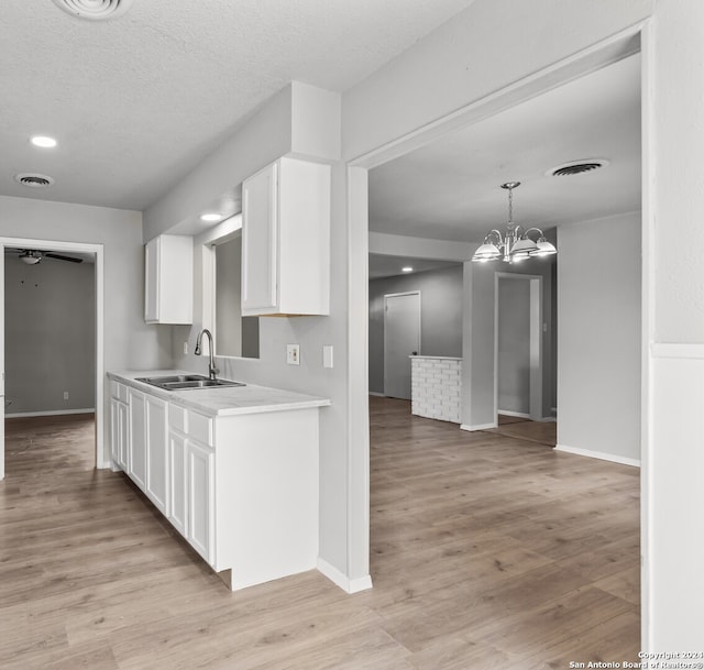 kitchen with hanging light fixtures, sink, a textured ceiling, white cabinetry, and light wood-type flooring