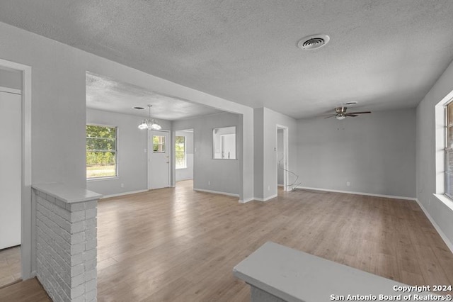 unfurnished living room featuring ceiling fan with notable chandelier, a textured ceiling, and light hardwood / wood-style flooring